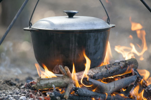Camping kettle over burning campfire in forest.